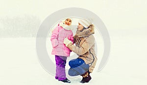Happy smiling mother and little girl child walking together in winter park outdoors on snowy background