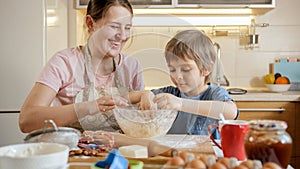 Happy smiling mother with little son kneading and smelling dough in glass bowl. Children cooking with parents, little