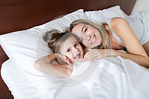 Happy smiling mother lying in bed with little jocund daughter.