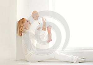 Happy smiling mother playing with baby home in white room nea