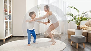 Happy smiling mother playing and dancing with her little son in living room at home. Family having fun together, listening music,