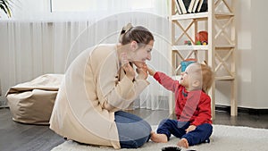 Happy smiling mother playing with her cute baby son on carpet in living room
