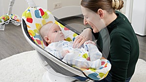 Happy smiling mother playing with her little baby son sitting in electric rocking chair at home. Child development and