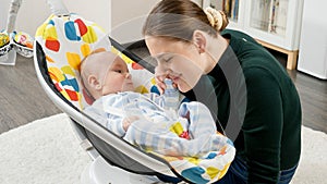 Happy smiling mother playing with her little baby son sitting in electric rocking chair at home. Child development and