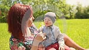 Happy smiling mother and son child sitting on grass and play with dandelion outdoor