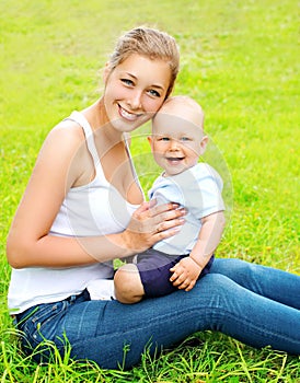 Happy smiling mother and son child sitting on grass in summer