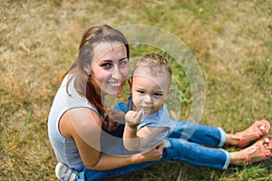 Happy smiling mother and son child sitting on grass in summer day