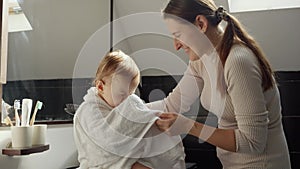 Happy smiling mother wiping her baby son in bath with towel and combing his hair.