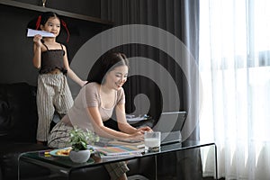 Happy smiling mother working remotely and spending time cute little daughter at home