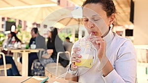 Happy smiling multi ethnic woman drinking healthy juice from straw, sitting in outdoor cafe