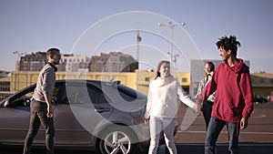 Happy, smiling multirace young two couples get out from the car and walking by parking zone near the malls around. Two