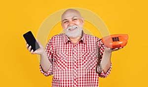 happy smiling old man with retro telephone and modern smartphone on yellow background