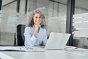 Happy middle aged business woman working on laptop in office, portrait.