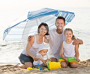 Family sitting under umbrella on the beach.