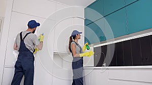 Happy smiling people of the cleaning office wipping the kitchen furniture with spray and rags