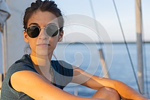 Happy smiling portrait of a beautiful young girl in sunglasses on a yacht or boat on the coast with the sea in the background
