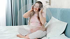 Happy smiling pregnant woman with big belly enjoys listening music in headphones. Unborn baby listening to classic music