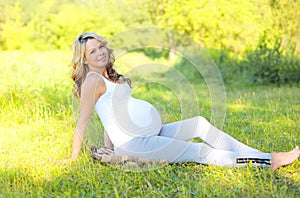 Happy smiling pregnant woman outdoors on grass in sunny summer