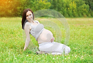 Happy smiling pregnant woman resting on grass in summer