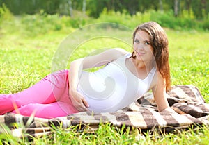 Happy smiling pregnant woman resting lying on grass in summer