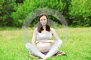 Happy smiling pregnant woman sitting on grass doing yoga in summer