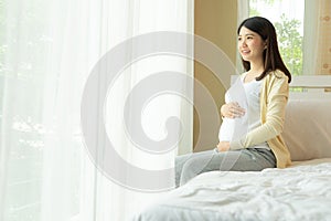 Happy smiling pregnant woman touching belly sitting in bed at home