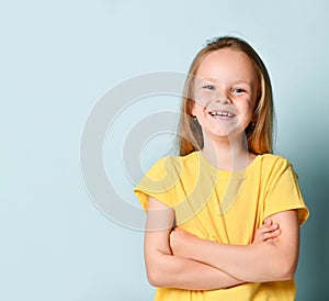 Happy smiling preschool girl with long blond hair posing with hands crossed on his chest. Waist up portrait isolated on blue, copy