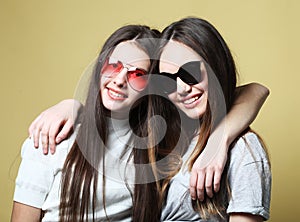 Happy smiling pretty teenage girls wearing sunglasses hugging over yellow background