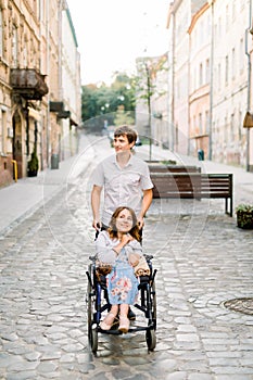 Happy smiling pretty woman in wheelchair and young handsome man at the old city center on sunny day