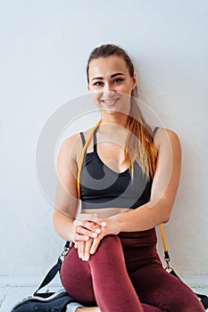 Happy, smiling, pumped up, athletic girl sitting on the floor, near a wall. She is happy with compleating the training. In her