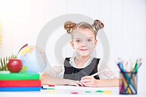Happy smiling pupil at the desk. Girl in the class room with pen