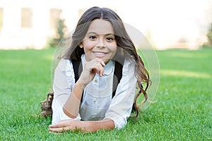 Happy smiling pupil. Girl cute kid laying green grass. Happy kid relaxing outdoors. Girl school uniform enjoy relax