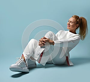 Happy smiling red-haired woman with ponytail hairstyle in white trendy casual pantsuit, kimono style sits on floor