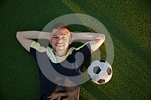 Happy smiling restful football player lying on green field grass