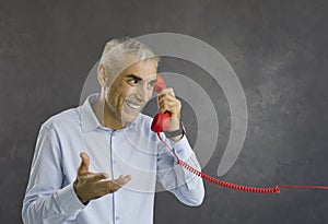 Happy smiling retired senior man talking to someone on red retro landline telephone