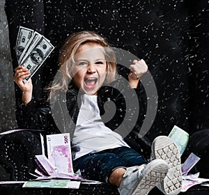 Happy smiling rich kid girl millionaire sitting in expensive armchair with a bundle of money dollars cash bills show winning sign photo