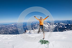 Happy smiling rope team man with climbing axe dressed orange mountaineering clothes,boots with crampons and safety harness rised a