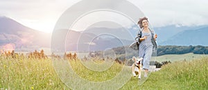 Happy smiling running beagle dog portrait with tongue out and owner female jogging by the mounting meadow grass path. Walking in