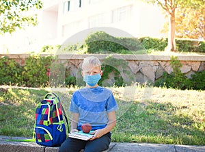 Happy smiling schoolboy on the background of school. School boy wearing medical face mask to health protection. Back to school.