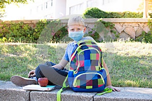 Happy smiling schoolboy on the background of school. School boy wearing medical face mask to health protection. Back to school.