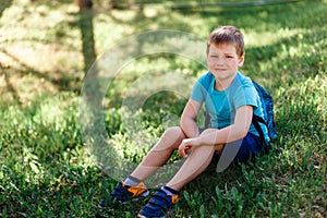 Happy smiling schoolboy with backpack sitting on green grass