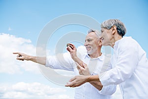 happy smiling senior couple holding stone and pointing with finger under blue sky.