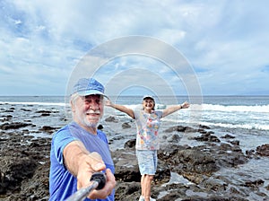 Happy smiling senior couple in retirement enjoying sunny day at sea while taking self portraits together with a smartphone and