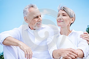 happy smiling senior couple in white shirts embracing under blue sky.