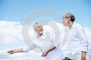 happy smiling senior couple in white shirts looking at each other under blue sky.