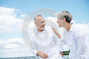 happy smiling senior couple in white shirts looking at each other under blue sky.