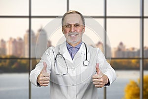 Happy smiling senior doctor shows both thumbs up.