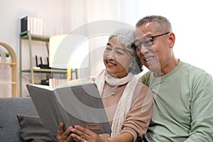 Happy smiling senior family couple in love reading book together, hugging embracing while spending free time at home on retirement