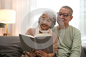 Happy smiling senior family couple in love reading book together, hugging embracing while spending free time at home on retirement