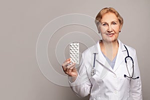 Happy smiling senior female doctor showing pills. Medicine and health care concept